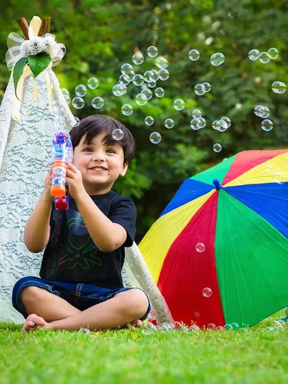 The simple magic of childhood captured outdoors. A young boy's face is full of delight as he plays with bubbles in a beautiful green park, showcasing the beauty of natural light photography.