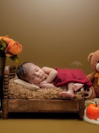A cozy autumn-themed shot of a newborn sleeping on a tiny bed next to a large teddy bear, a lantern, and pumpkins.