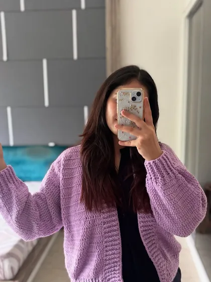 This is a mirror selfie showing the fit of our Plum Puff Cardigan in lavender. It has a comfortable, slightly oversized feel that fits a range of sizes from S to XL.