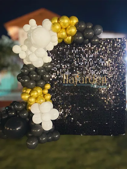 A simple yet striking outdoor setup featuring a black sequin wall. The partial balloon garland in black, white, and gold adds a touch of modern elegance.