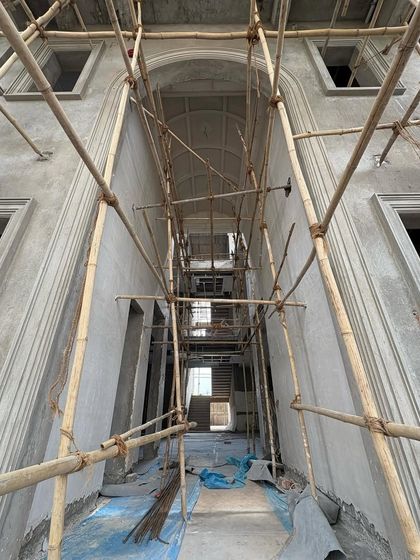 The skeleton of a grand, arched hallway, revealed by the scaffolding. This low-angle shot emphasizes the height and architectural ambition of the space, which will soon be a refined and elegant corridor.