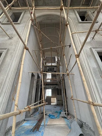 The skeleton of a grand, arched hallway, revealed by the scaffolding. This low-angle shot emphasizes the height and architectural ambition of the space, which will soon be a refined and elegant corridor.