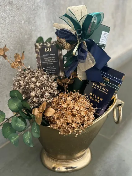A sophisticated gift for a gentleman's 60th birthday. This champagne bucket holds premium spirits and is decorated with dried florals and masculine accents in a deep green and gold color palette.