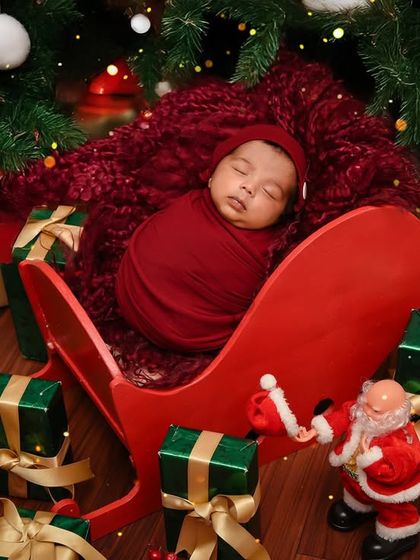 A festive Christmas-themed newborn shoot, with the baby sleeping in a miniature sleigh surrounded by presents under a Christmas tree. Perfect for holiday babies.