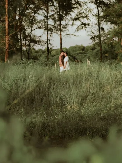 A couple stands together in a field of tall grass, sharing a quiet, intimate moment. This photo captures the feeling of finding your own world together, surrounded by nature.