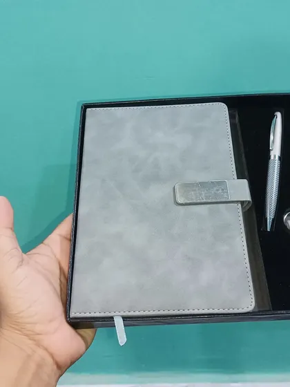 This gift set includes a personalized grey leather diary with a nameplate, a matching keychain, and a pen, all held in my hand to show the size.