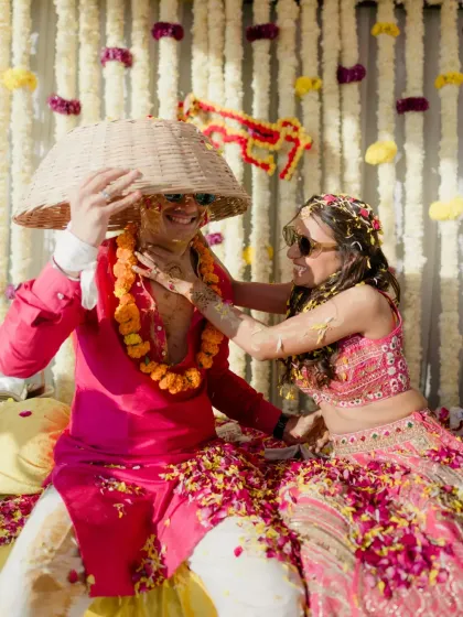 A playful moment during the Haldi, where the couple shares a laugh under a makeshift hat, surrounded by petals and joy.