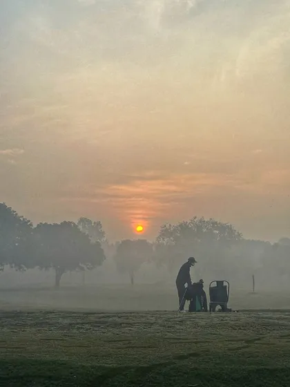 A beautiful, hazy sunrise creates a mystical atmosphere for the early morning golfers.