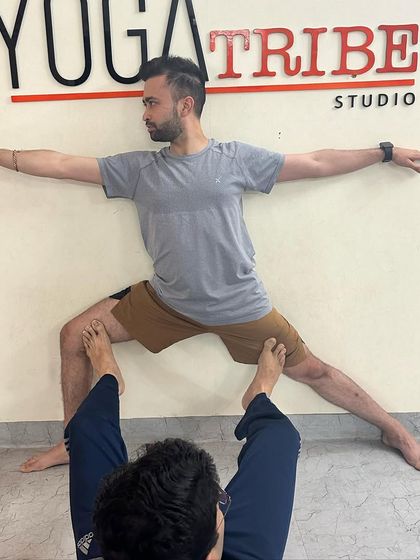 A student acts as a base to help his partner find the correct alignment in Virabhadrasana II (Warrior II), a creative and effective partner adjustment.
