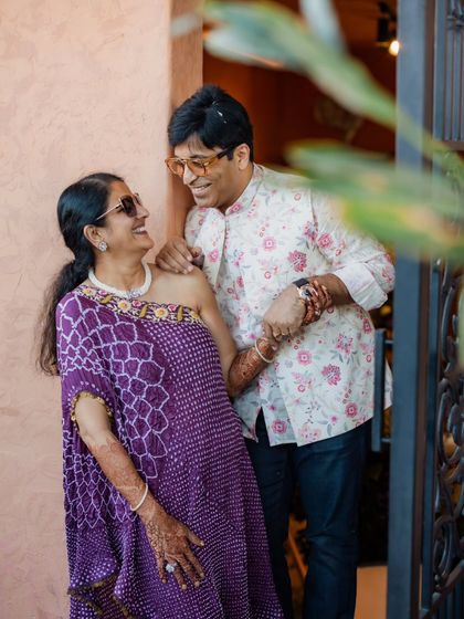 A fun, candid moment between family members at the Haldi. We styled them in comfortable yet stylish outfits, like this purple bandhani one-shoulder top and a floral print Nehru jacket, perfect for a relaxed daytime event.