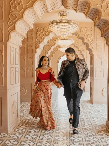A happy, candid moment as an expecting couple walks hand-in-hand through an ornate, traditional Indian corridor. Their coordinated Indo-western outfits add a touch of cultural elegance to this natural, in-motion maternity photograph.