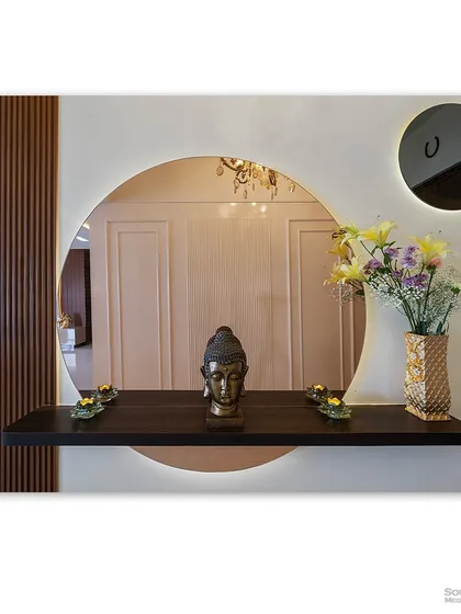 A modern foyer detail, featuring a circular mirror with backlighting and a simple wooden shelf. The Buddha head and fresh flowers create a welcoming and peaceful first impression.