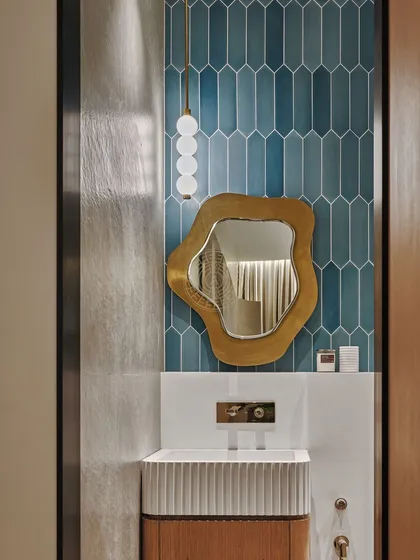 We used playful, elongated hexagonal blue tiles in this show apartment bathroom. The asymmetrical, organic-shaped mirror with a brass frame adds a fun and fresh touch.