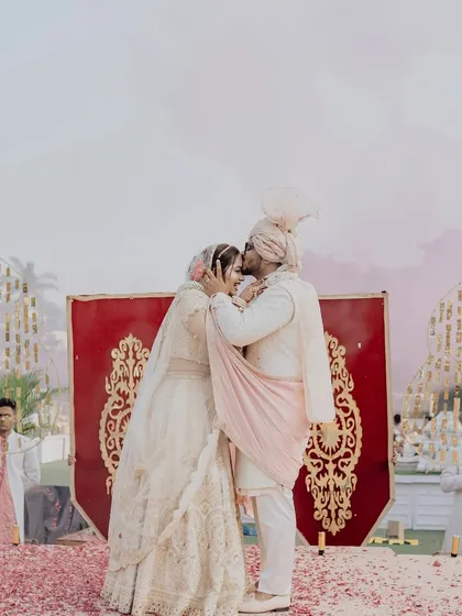 A sweet kiss shared on the varmala stage, surrounded by a carpet of red rose petals. These are the romantic moments that make all the planning worthwhile.