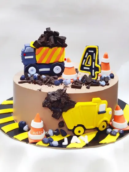 This all-edible JCB construction theme cake is perfect for a little builder. It features handcrafted fondant trucks, traffic cones, and chocolate "dirt" for a fun and interactive design.