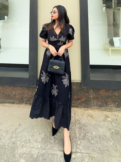 A full-length street style shot of the black embroidered dress, paired with classic black pumps and sunglasses. A chic and sophisticated city look.