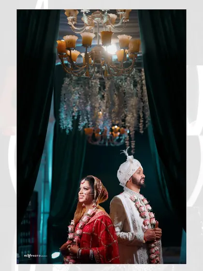 The bride and groom standing back-to-back under a magnificent chandelier after their wedding ceremony. This stylish portrait captures their stunning traditional attire and the opulence of the wedding decor.