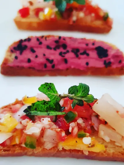 An assortment of gluten-free crostini with exciting toppings. One features a bright pink beetroot hummus, while the other is topped with a fresh and tangy pineapple salsa.