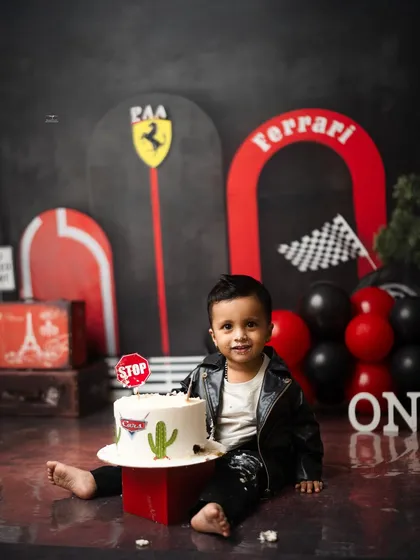 The birthday boy sits with his amazing race car-themed cake. The Ferrari setup is complete with a "Stop" sign topper, perfect for a little speed racer.