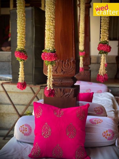 A close-up of the traditional seating, with bright pink block-printed cushions and hanging jasmine garlands adding to the festive decor.