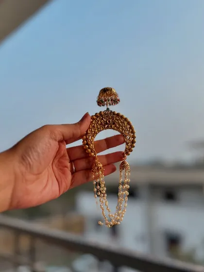 A traditional 'Khopa' hair accessory, designed to be worn on a hair bun. This piece, with its pearl chains and jhumka, adds a final touch of grace to a Maharashtrian look.