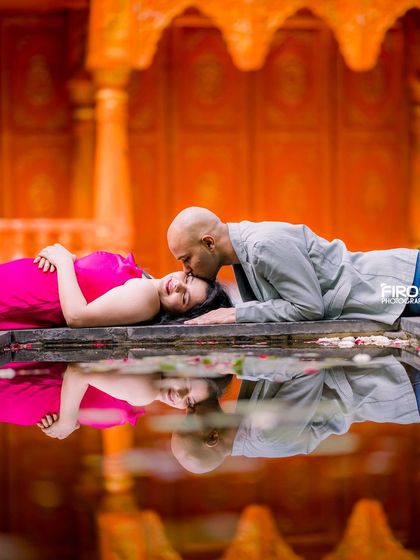 A tender moment with a reflection in the water, set against a vibrant orange Jaipuri-style backdrop.