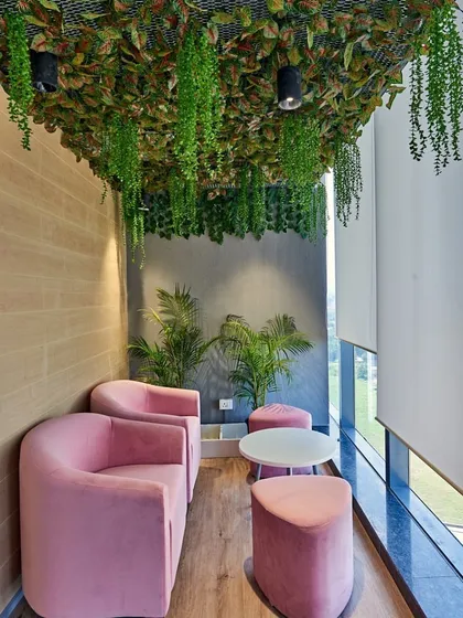 A cozy lounge nook with pink armchairs and a ceiling covered in artificial hanging plants, creating a lush, garden-like feel with a view.