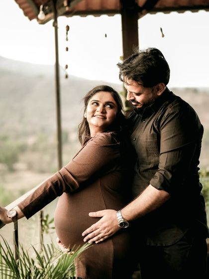 The couple shares an embrace on a balcony overlooking a beautiful view. It’s a quiet, loving moment of them together, looking towards the future.