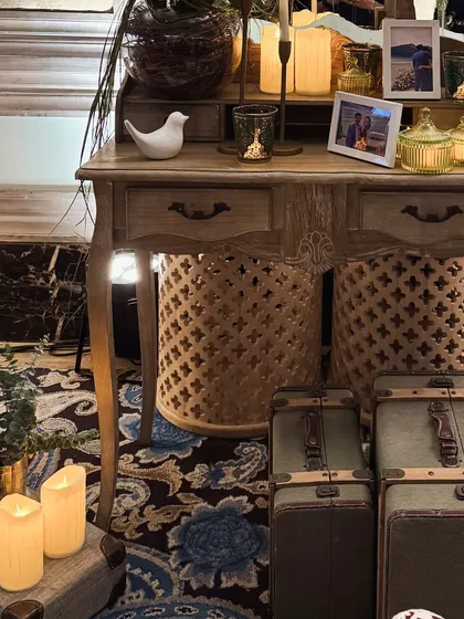 A vintage-inspired welcome lunch setup with stacked suitcases, a floral-printed lamp, and a beautifully arranged console table with books and candles.
