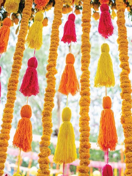 Details make the design. This backdrop features playful pink, yellow, and orange tassels hanging between elegant lines of marigold flowers, creating a perfect blend of charm and vibrancy.