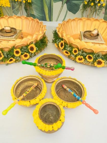The details of a Haldi ceremony setup. This image shows the traditional brass bowls ('urli') decorated with sunflowers, ready for the turmeric paste, blending functionality with beautiful aesthetics.