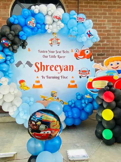 A "Little Racer" car-themed birthday party for a 5-year-old. The decoration includes a custom circular backdrop with race cars, a balloon arch in blue, black, and white, and a traffic light balloon sculpture.