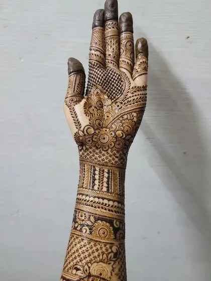 A full view of a detailed bridal henna design, extending from the fingertips to the mid-forearm. This piece combines floral patterns, checks, and bold bands for a traditional yet clean look.