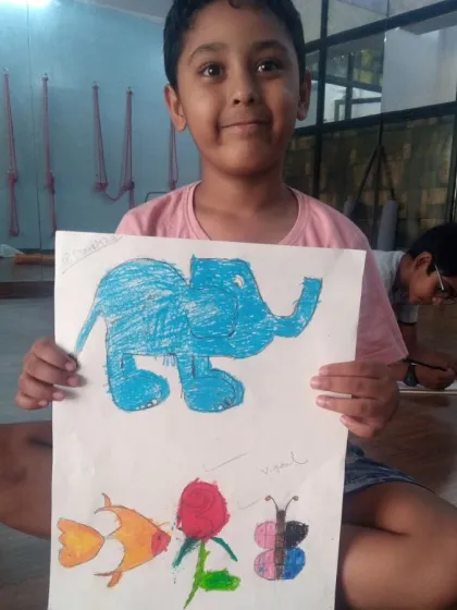 Heetkarsh, a 6-year-old student, shows his drawings of an elephant, fish, and flower. Using oil pastels, he is learning to draw different forms from nature.