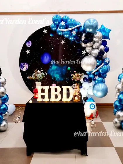 A simple yet effective space theme, using a circular galaxy backdrop, two balloon pillars, and a table for the cake.