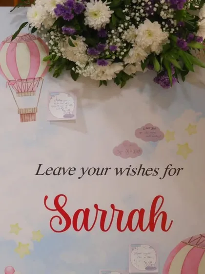 A "Leave your wishes" board for guests to write personal messages for the birthday girl. The board is decorated with a hot air balloon theme and topped with fresh flowers.