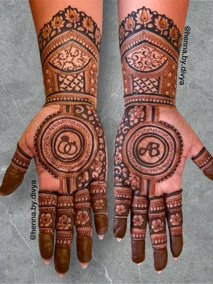 This engagement mehendi features the couple's initials 'AB' and an engagement ring symbol inside matching mandalas. The design is symmetrical and filled with traditional floral work.