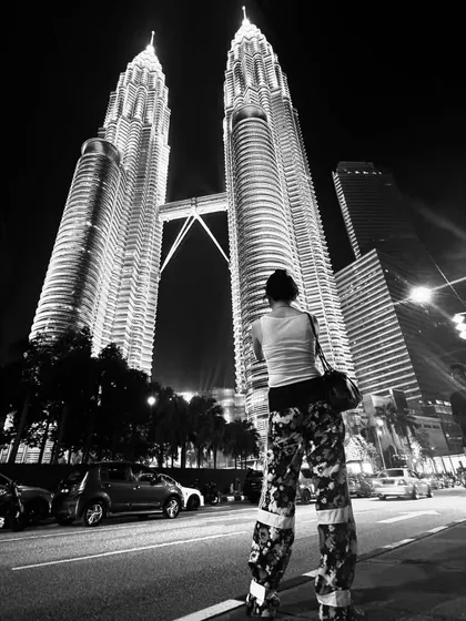My custom floral print pants against the backdrop of Kuala Lumpur's modern architecture. The wide-leg, high-contrast design stands out, especially in a dramatic, monochrome night setting.