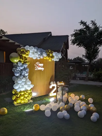 The outdoor birthday decoration viewed from the side, highlighting the depth of the balloon arch against the wooden backdrop.