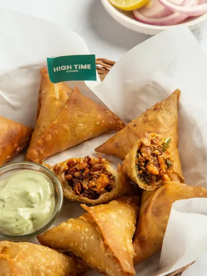 A close-up on the vegan samosas, focusing on the crispy pastry and the texture of the plant-based filling. The fresh dip on the side adds a pop of color and suggests a perfect pairing.
