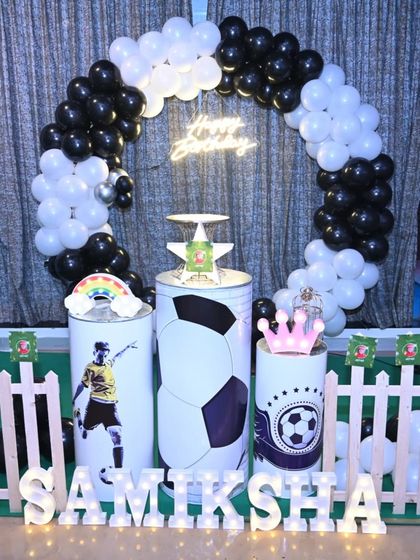 A football-themed birthday setup perfect for a young athlete. The decoration includes a black and white balloon ring, custom pedestals with football graphics, and a bright neon sign.