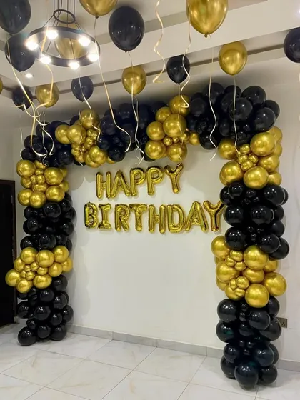 A classic black and gold birthday decoration. This setup includes a large organic balloon arch and 'Happy Birthday' foil letters, creating a timeless and celebratory look suitable for any age.