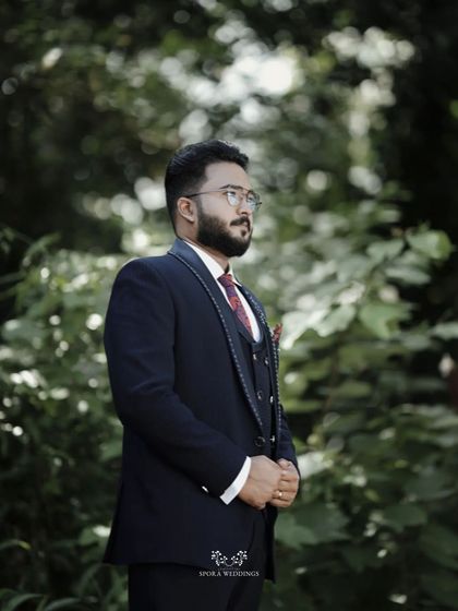 The groom in a classic pose, looking thoughtful and elegant in his wedding suit amidst a natural setting.