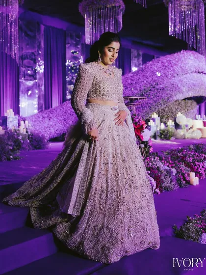A bride looking ethereal amidst a sea of purple, the theme color of her grand reception. The decor and lighting are as much a part of the story as the couple themselves.