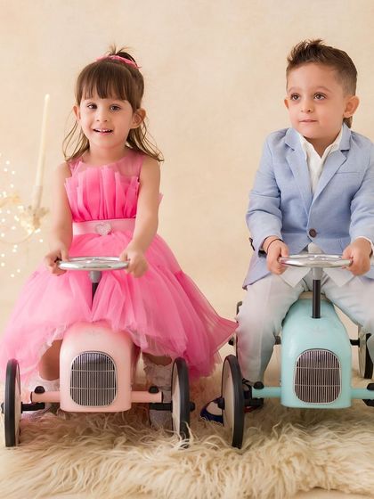 A playful portrait of a brother and sister on vintage-style toy cars. Their coordinated outfits and the fun props make for a unique photo.