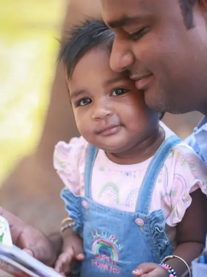 A sweet father-daughter moment during an outdoor shoot, with the baby looking curiously at the camera while cuddled in her dad's arms.