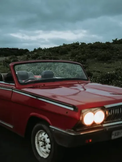 The couple shares an embrace in their vintage car as dusk settles, with the headlights on. This creates a moody, cinematic, and incredibly romantic atmosphere.