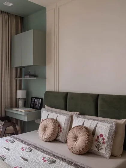 The 'after' shot of the guest bedroom. The combination of a dark green headboard with soft-toned bedding and a compact study desk creates a welcoming and functional space.