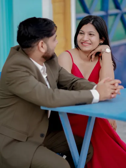 A playful moment sharing a drink against a vibrant blue door, reminiscent of a European street. The woman's bright red dress pops against the cool tones, creating a lively and stylish pre-wedding photo.