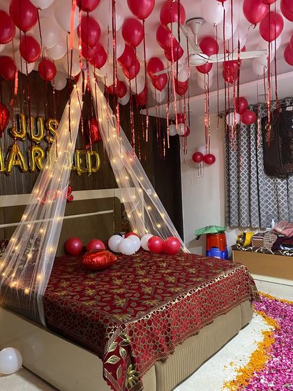 This image shows a full "Just Married" decoration with a petal pathway, ceiling balloons, and a lit canopy over a traditionally decorated bed.